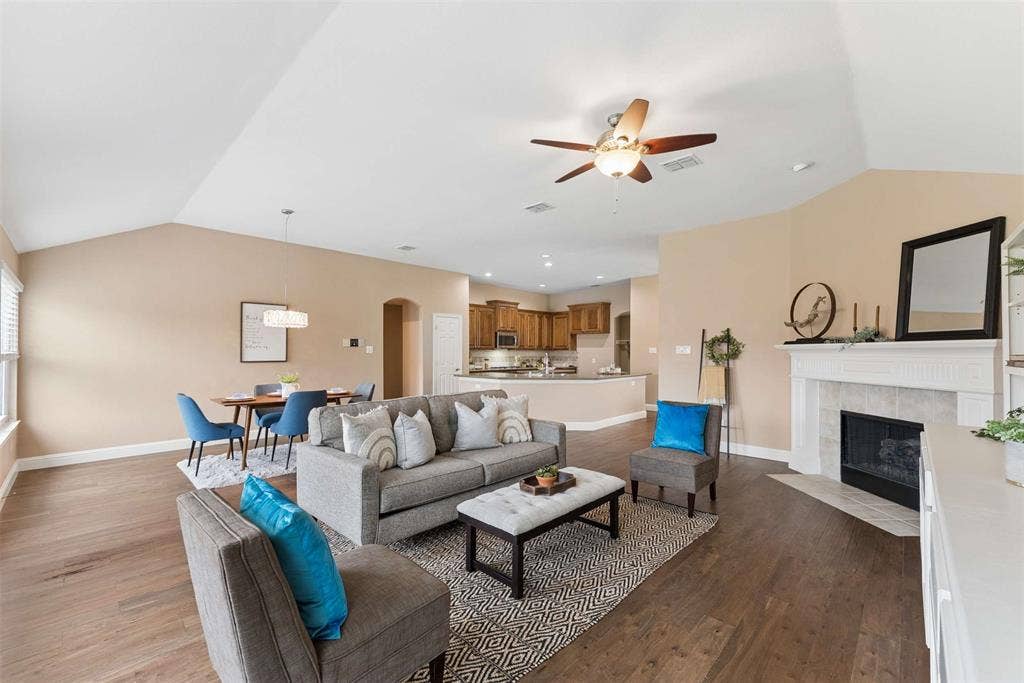 1221 Amistad Drive, Prosper, TX 75078 The living area features vaulted ceilings, dark wood floors, and an elegant fireplace with a white mantle