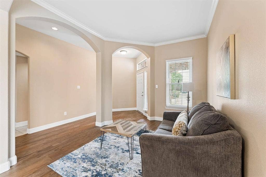 1221 Amistad Drive, Prosper, TX 75078 Living area featuring warm neutral wall tones, crown molding, and wood-look flooring