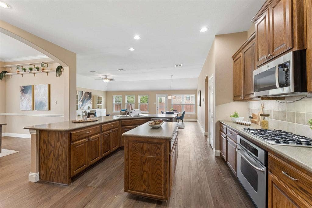 1221 Amistad Drive, Prosper, TX 75078 The kitchen features wood cabinetry, a central island, and stainless steel appliances including a microwave, oven, and gas cooktop