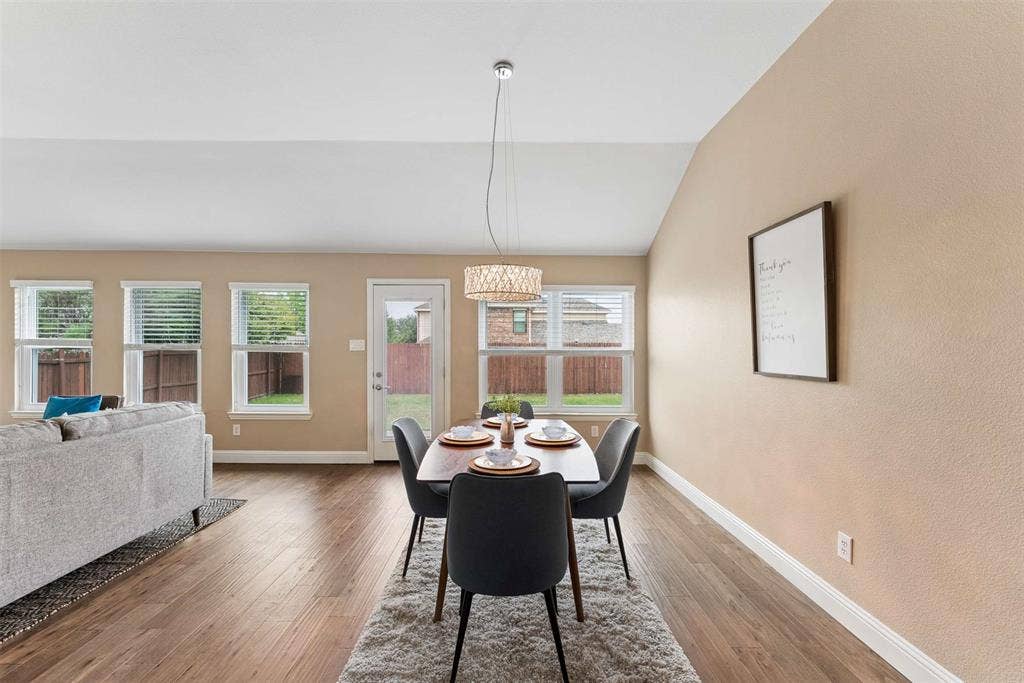 1221 Amistad Drive, Prosper, TX 75078 The property features an open-concept living and dining area with wood flooring and a vaulted ceiling