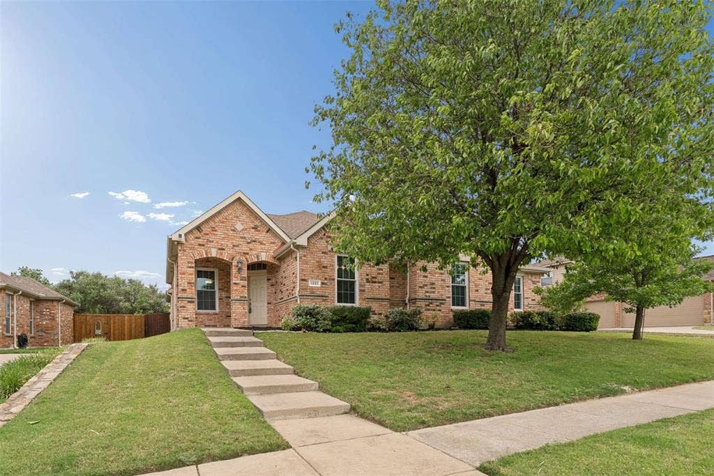 1221 Amistad Drive, Prosper, TX 75078 The property features a brick exterior, a well-maintained lawn, and mature trees