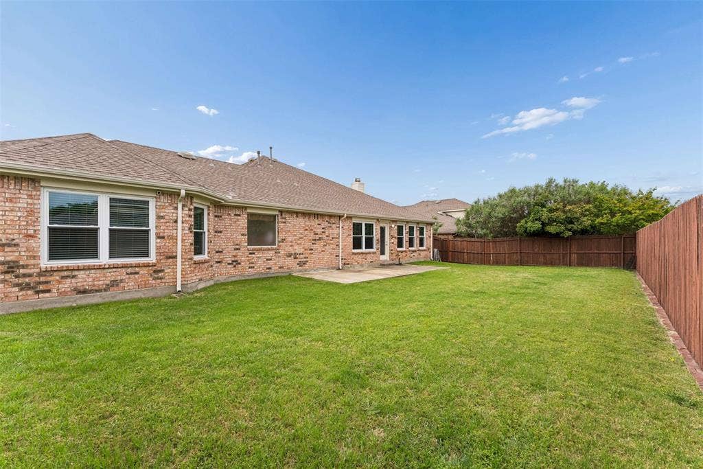 1221 Amistad Drive, Prosper, TX 75078 The property features an extensive lawn area, a brick exterior, and a brown privacy fence