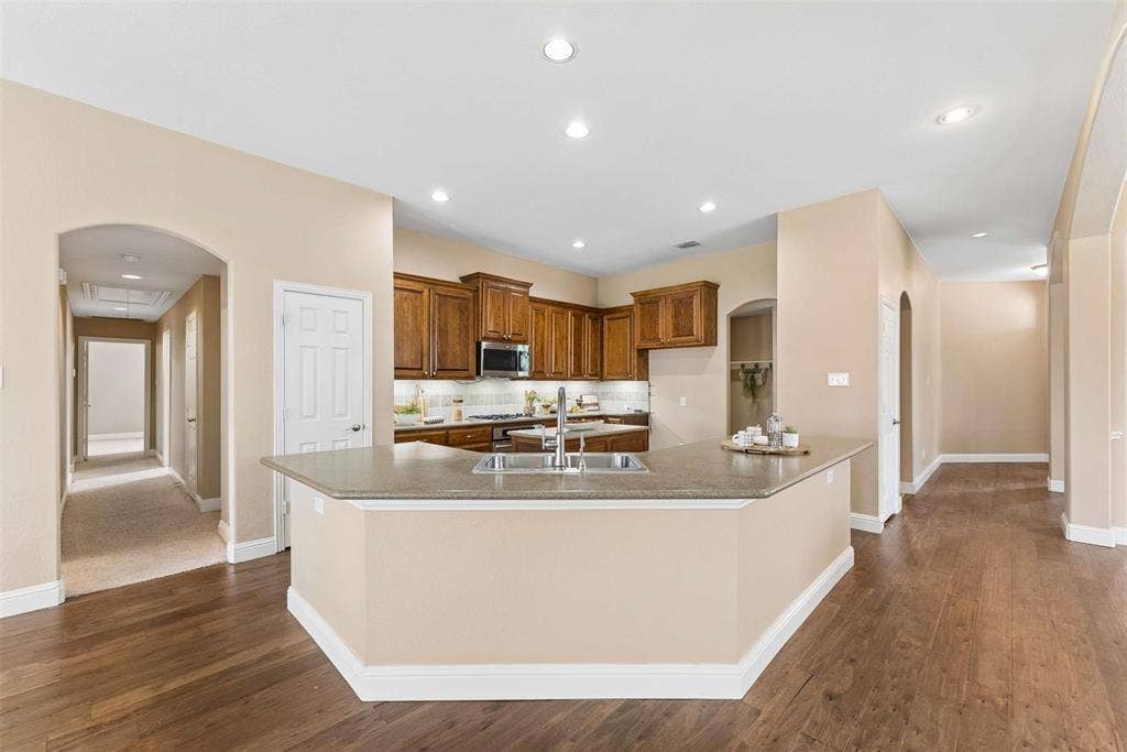 1221 Amistad Drive, Prosper, TX 75078 The kitchen features wood cabinetry, stainless steel appliances, and a central island with a double sink and granite countertops