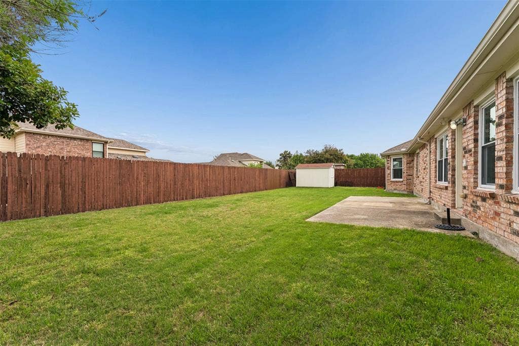 1221 Amistad Drive, Prosper, TX 75078 The property features a spacious lawn, a privacy fence, and a concrete patio