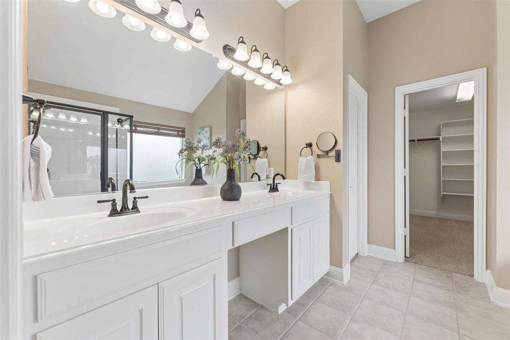 1221 Amistad Drive, Prosper, TX 75078 The bathroom features a double vanity with white cabinetry, a large mirror with overhead lighting, and tiled flooring