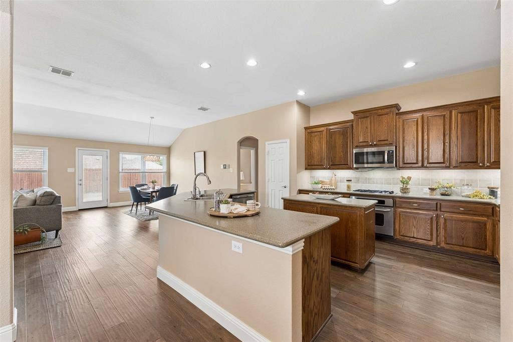 1221 Amistad Drive, Prosper, TX 75078 The open concept living area features hardwood floors, recessed lighting, and a kitchen island with a sink