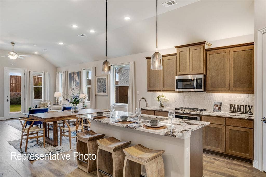 1415 Odette Drive, Arlington, TX 76013 The open-concept living area features a kitchen with light wood cabinetry, a large kitchen island with a granite countertop, and stainless steel appliances