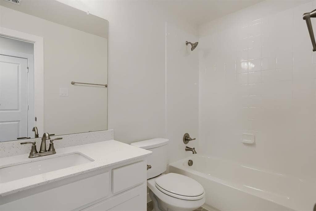 828 Stone Grove Road, Lavon, TX 75166 Bathroom featuring a white vanity with an integrated sink, a speckled light-toned countertop, a frameless wall mirror, and a white bathtub with a tiled surround