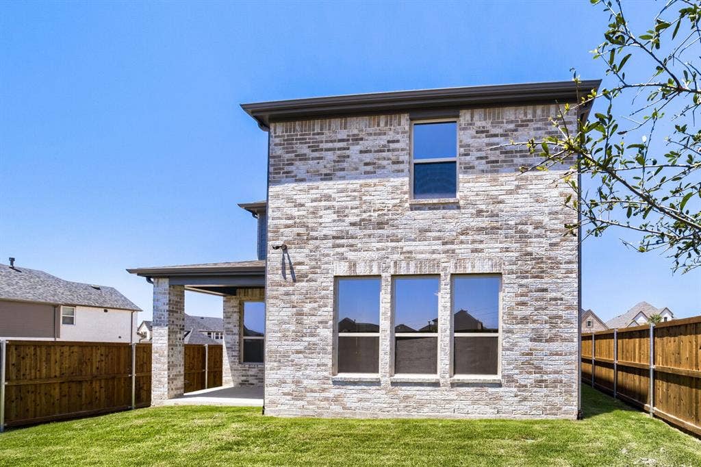 828 Stone Grove Road, Lavon, TX 75166 Brick veneer exterior with a covered patio, three ground-floor windows, an upper-level window, and a wood privacy fence