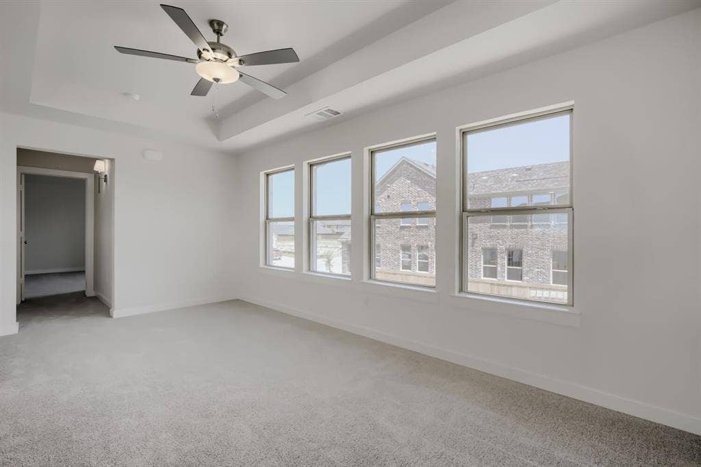 828 Stone Grove Road, Lavon, TX 75166 Spacious interior room featuring a tray ceiling, contemporary ceiling fan, light gray carpet, and a row of four windows