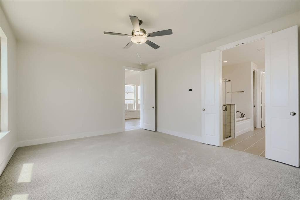 828 Stone Grove Road, Lavon, TX 75166 Carpeted room featuring a ceiling fan with integrated lighting, a window, and two paneled doors opening to a bathroom with a glass-enclosed shower and a bathtub