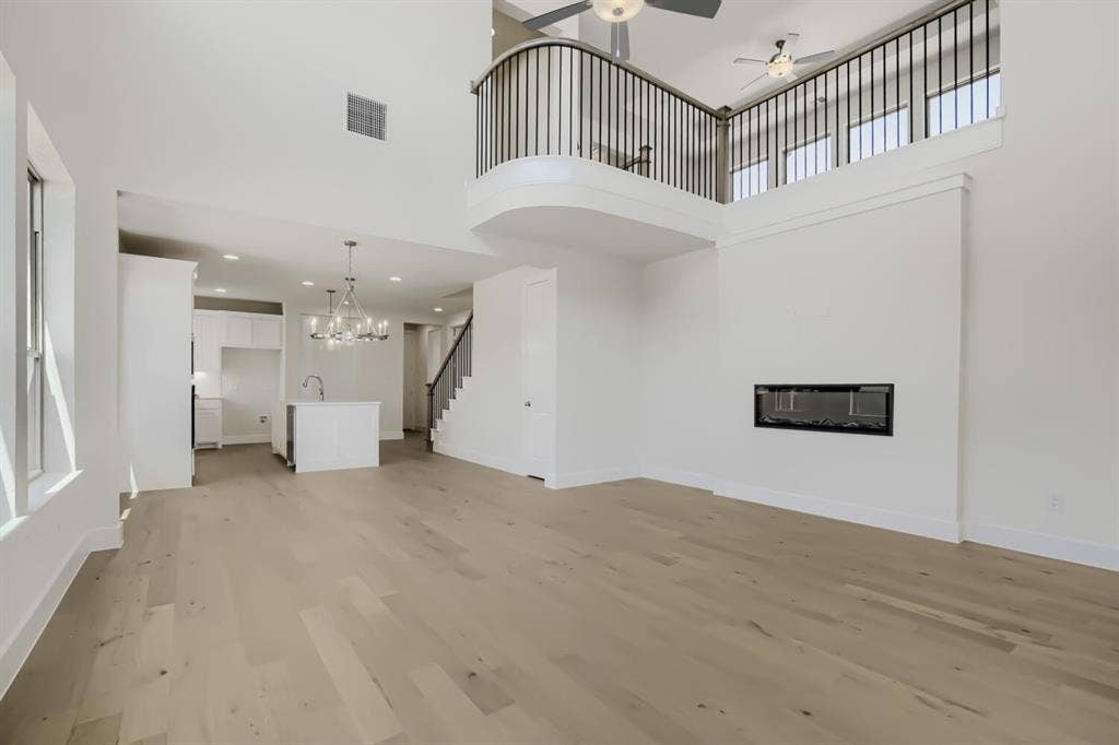 828 Stone Grove Road, Lavon, TX 75166 Open-concept interior featuring light wood-finish flooring, a contemporary fireplace, a kitchen island with a sink and chandelier, a staircase with dark railings, and a second-story balcony with dark balusters