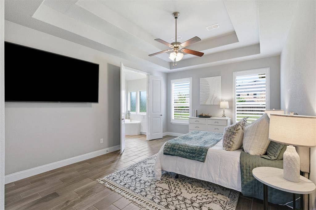 11414 Alejandra Lane, Frisco, TX 75035 Spacious primary bedroom featuring wood-finish tile flooring, a tray ceiling with a ceiling fan, and white plantation shutters on multiple windows