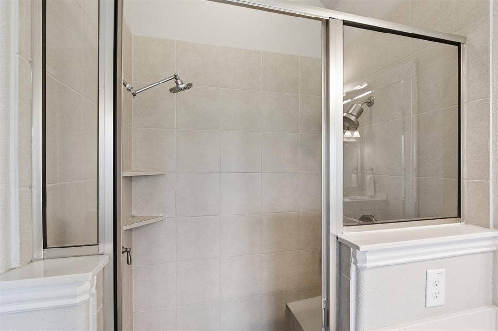 11414 Alejandra Lane, Frisco, TX 75035 Enclosed shower with a glass sliding door, large format tile surround, built-in corner shelving, a rain shower head, and an integrated bench