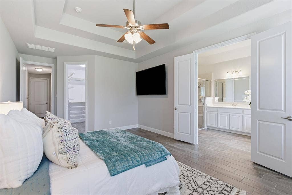 11414 Alejandra Lane, Frisco, TX 75035 Spacious bedroom featuring tray ceilings with a ceiling fan, light gray wall paint, and wood-finish flooring