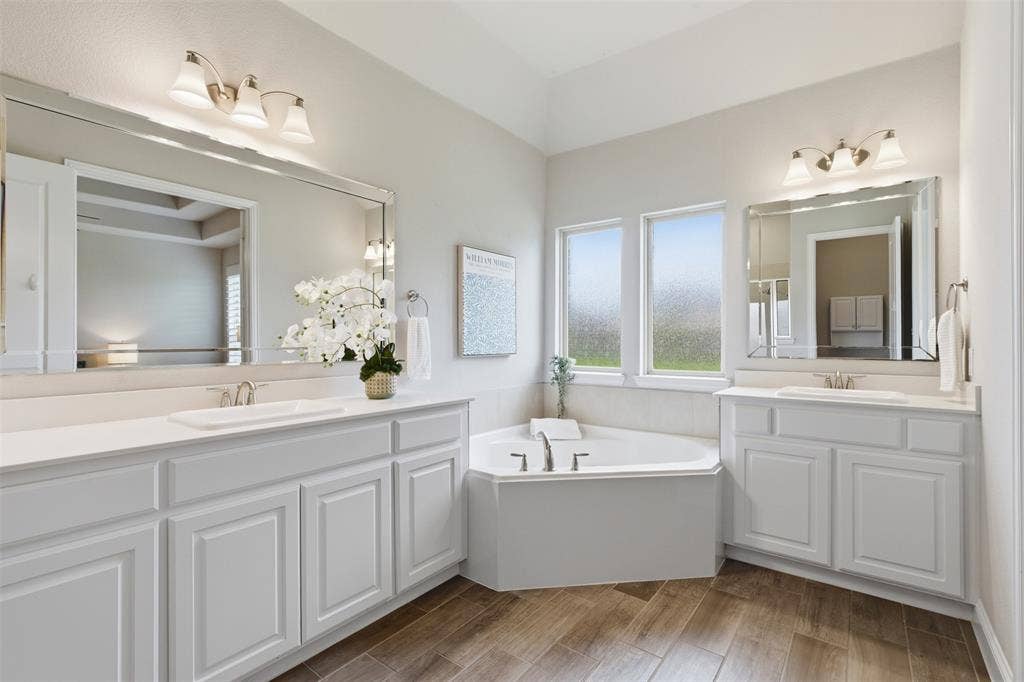 11414 Alejandra Lane, Frisco, TX 75035 Bathroom featuring a corner soaking tub, dual white vanities with undermount sinks, and wood-finish flooring