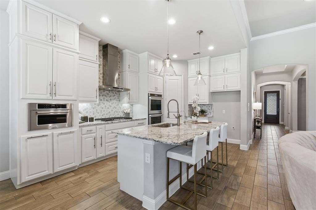 11414 Alejandra Lane, Frisco, TX 75035 Modern kitchen featuring an expansive center island with seating, white shaker cabinetry, stainless steel appliances, and wood-finish tile flooring