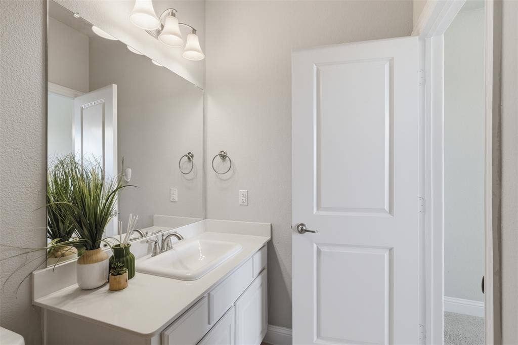 11414 Alejandra Lane, Frisco, TX 75035 Bathroom vanity featuring a white countertop with an integrated sink, brushed nickel faucet, and a large wall-mounted mirror