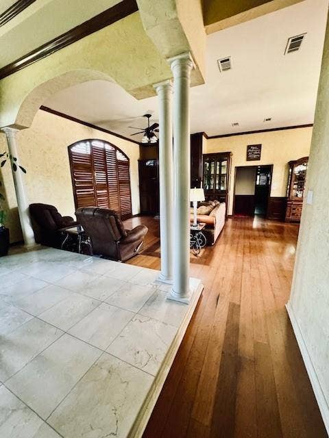 Corridor featuring hardwood / wood-style flooring, visible vents, ornate columns, and ornamental molding