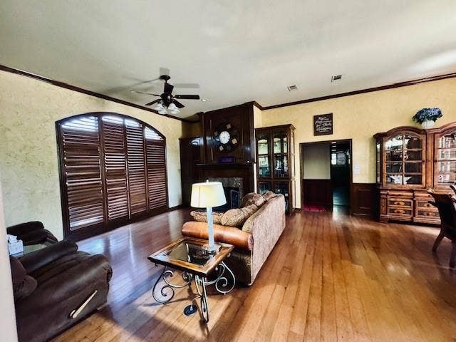 Living area featuring crown molding, a ceiling fan, visible vents, hardwood / wood-style floors, and wainscoting