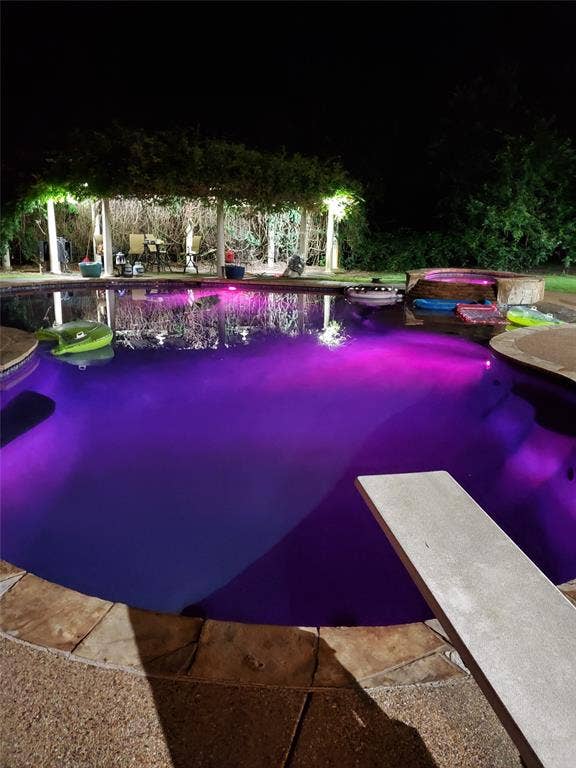 Pool at night featuring a diving board and an outdoor pool