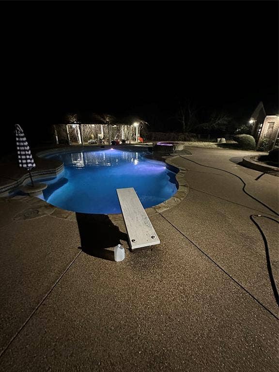 Pool at twilight featuring a diving board, an outdoor pool, and a patio area