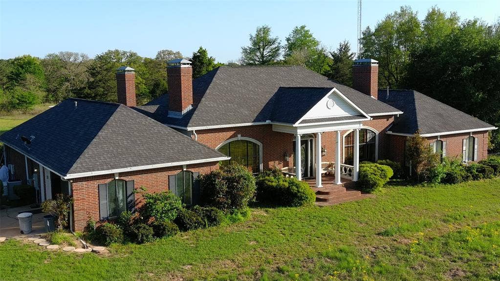 View of front facade featuring a chimney, brick siding, covered porch, and a front yard