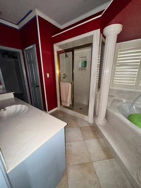 Bathroom with crown molding, a shower stall, decorative columns, and a garden tub