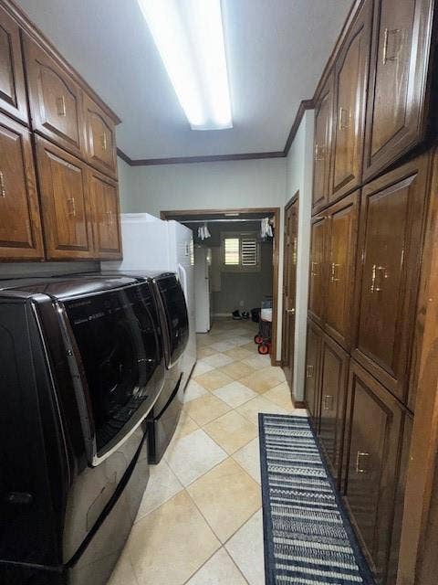 Clothes washing area featuring light tile patterned floors, independent washer and dryer, ornamental molding, and cabinet space