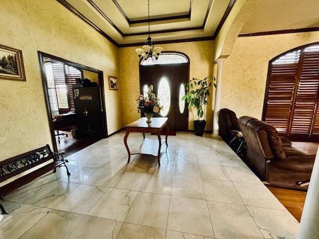 Entrance foyer with a textured wall, a notable chandelier, ornamental molding, and a raised ceiling