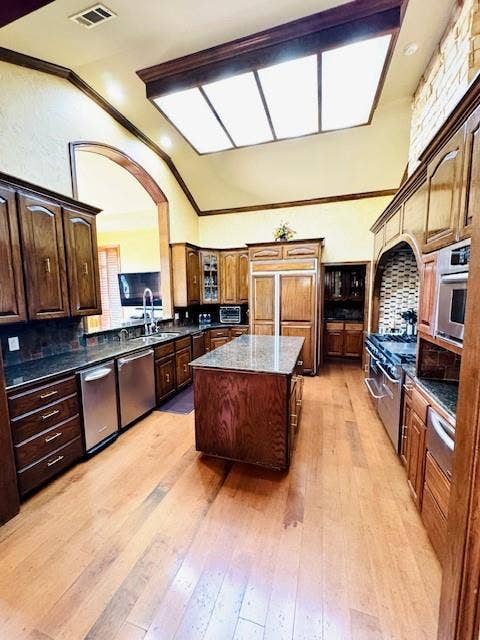 Kitchen featuring visible vents, a center island, light wood-style floors, high end appliances, and vaulted ceiling