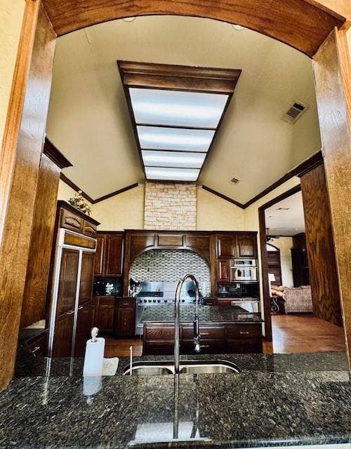 Kitchen with visible vents, a sink, dark brown cabinets, dark stone counters, and vaulted ceiling