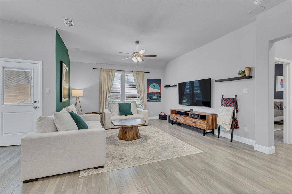 1000 Westwood Lane, Argyle, TX 76226 The property features a spacious living area with light-toned flooring, a vaulted ceiling, and a ceiling fan