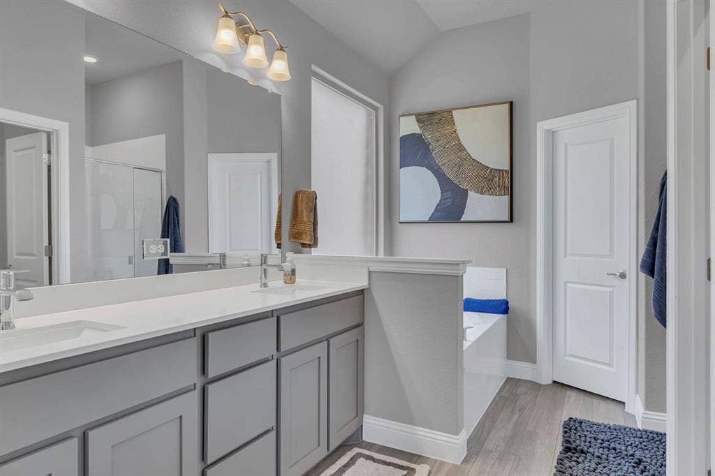 1000 Westwood Lane, Argyle, TX 76226 The bathroom features a dual vanity with light gray cabinetry and white countertops, a large mirror, and a built-in bathtub