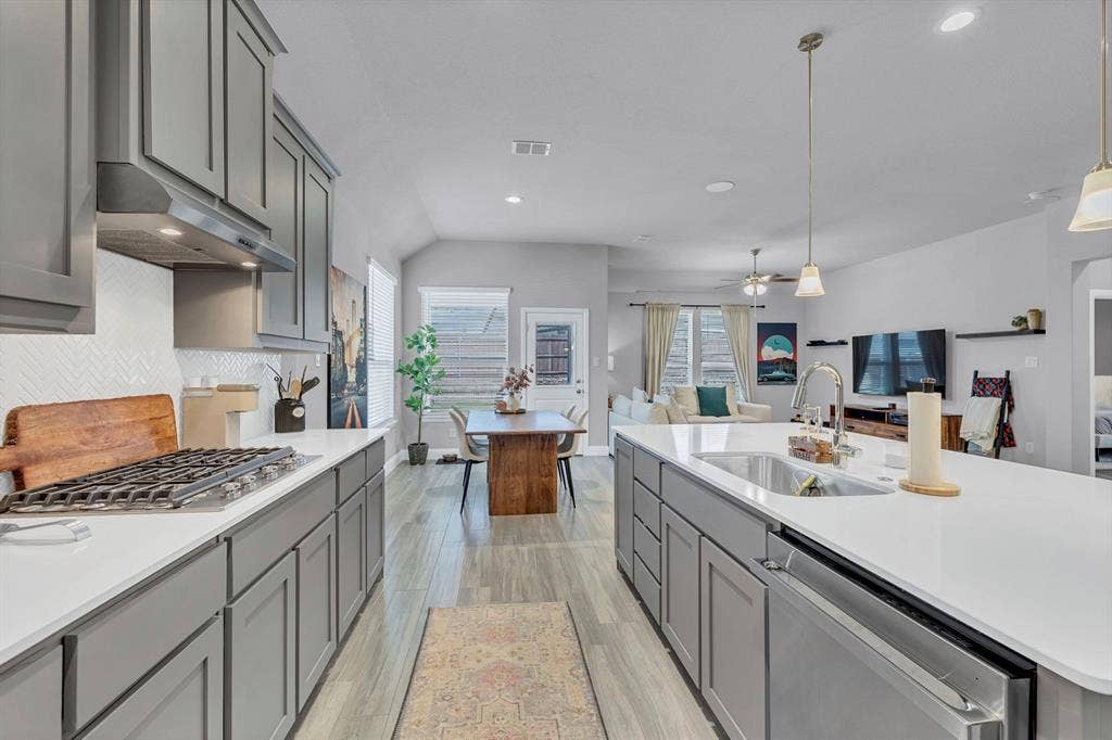 1000 Westwood Lane, Argyle, TX 76226 The kitchen features grey cabinetry, white countertops, a gas range with a range hood, and a built-in dishwasher