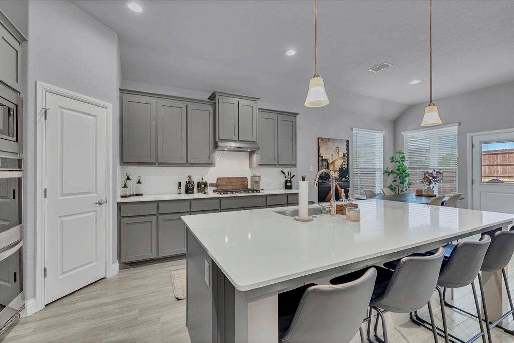 1000 Westwood Lane, Argyle, TX 76226 The kitchen features a large island with a sink, grey cabinetry, stainless steel appliances, and light-colored flooring