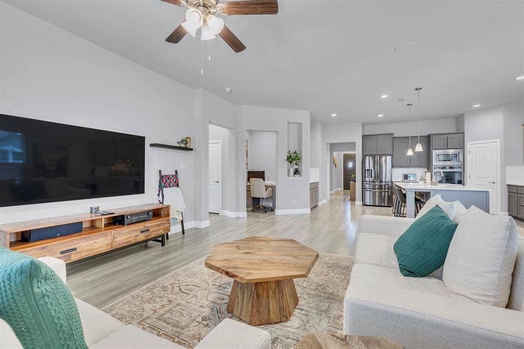 1000 Westwood Lane, Argyle, TX 76226 The open-concept living area features light-colored flooring, a ceiling fan, and recessed lighting, extending into a kitchen with grey cabinetry and stainless steel appliances