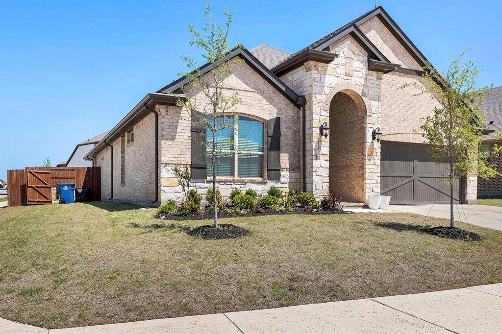 1000 Westwood Lane, Argyle, TX 76226 The property features a brick and stone exterior, an arched entryway, and an attached garage with a dark wood-style door