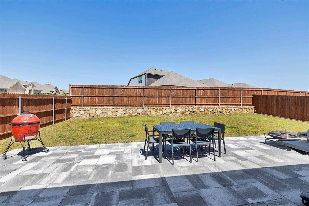 1000 Westwood Lane, Argyle, TX 76226 The property features an outdoor patio with varied rectangular pavers, a grassy yard, and a privacy fence set upon a stone retaining wall