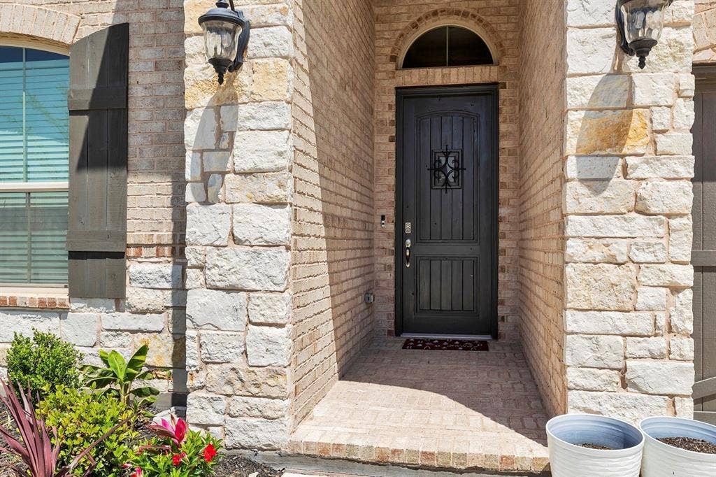 1000 Westwood Lane, Argyle, TX 76226 The property features an exterior of light-colored brick and stone, complemented by a dark entry door with an arched transom window