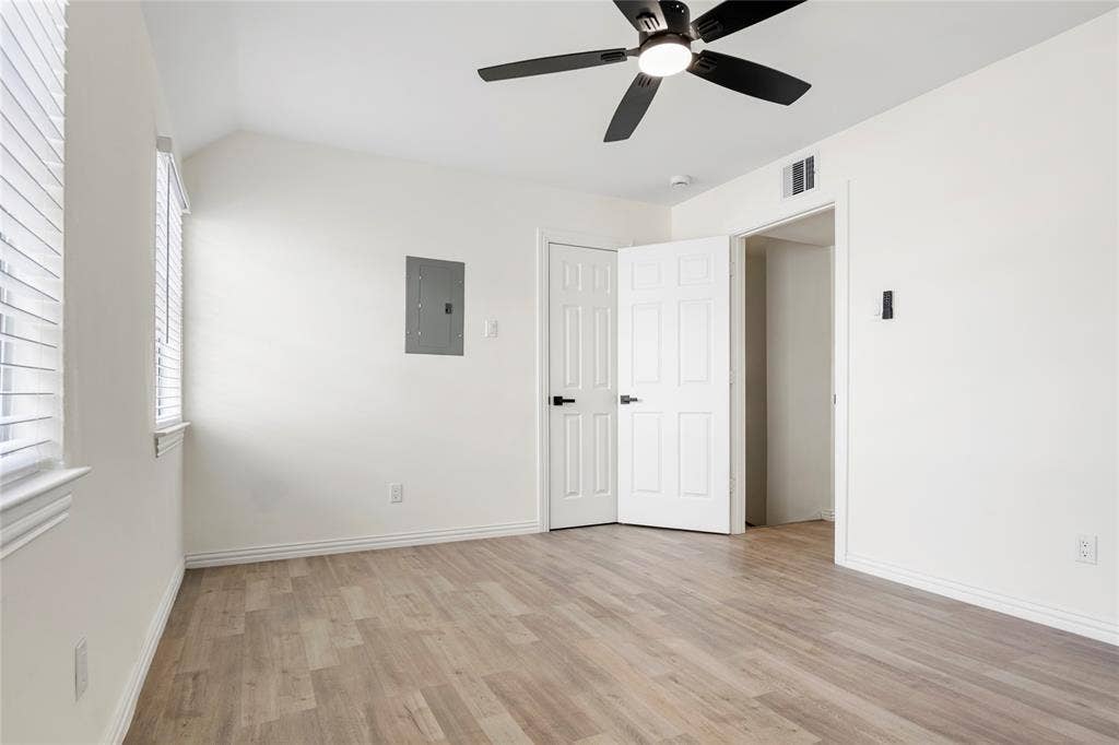 Room featuring light wood-finish flooring, white painted walls, and a black ceiling fan with integrated lighting