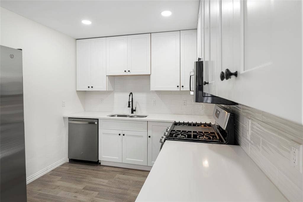 Contemporary kitchen featuring white shaker cabinetry, quartz countertops, subway tile backsplash, stainless steel appliances, and wood-finish flooring