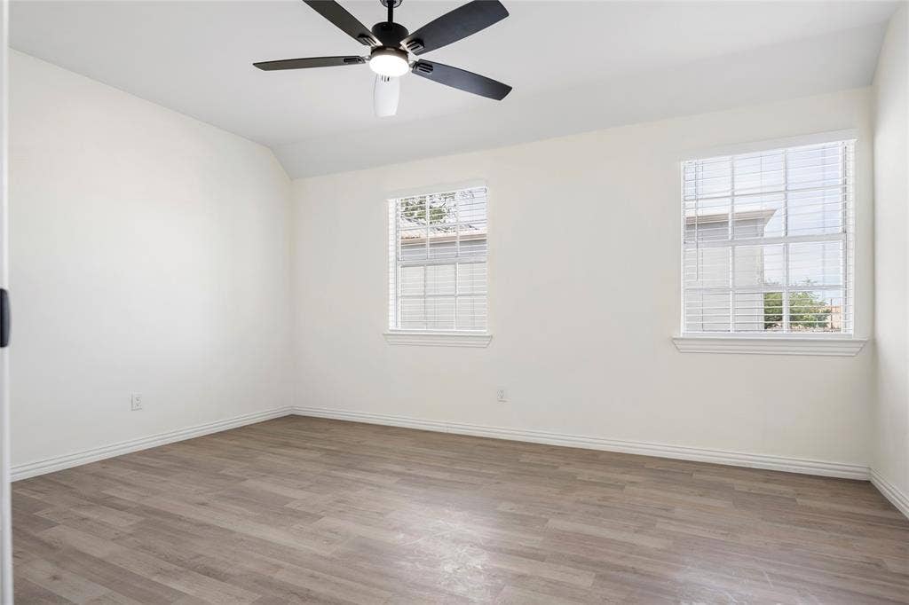 Spacious room featuring wood-finish flooring, white walls, and a ceiling fan with integrated lighting