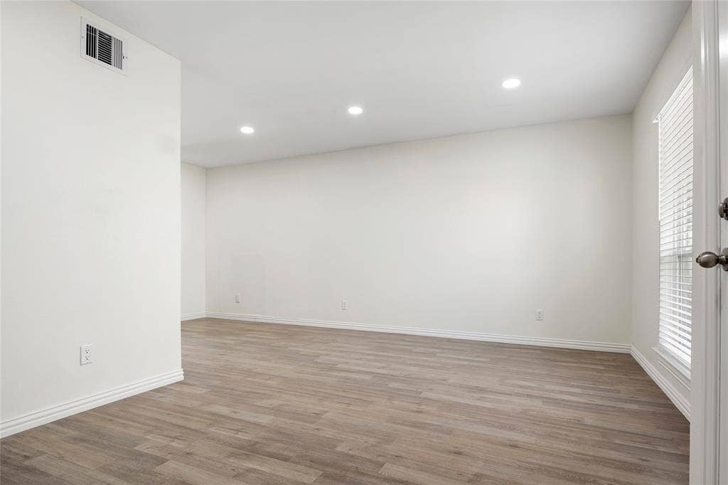 Spacious room featuring wood-finish flooring, white baseboards, recessed ceiling lighting, and a window with blinds