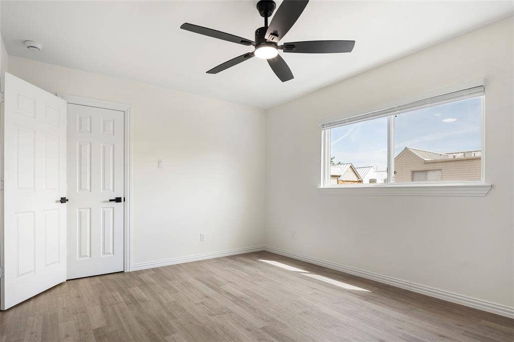 Bright room featuring a multi-pane window, wood-finish flooring, a modern black ceiling fan with integrated lighting, and white six-panel doors with matte black hardware