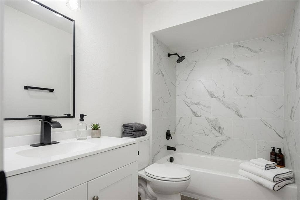 White single vanity with a solid surface countertop, matte black faucet, and rectangular mirror