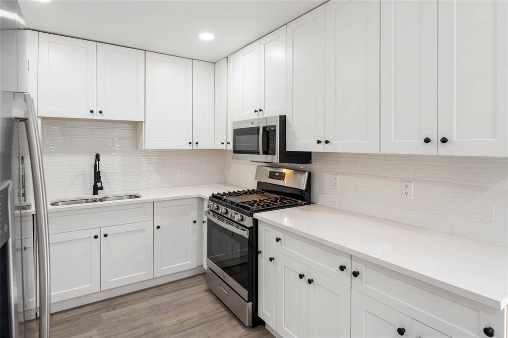 Kitchen featuring white shaker cabinetry, stainless steel appliances, a white tile backsplash, a matte black kitchen faucet, and wood-finish flooring