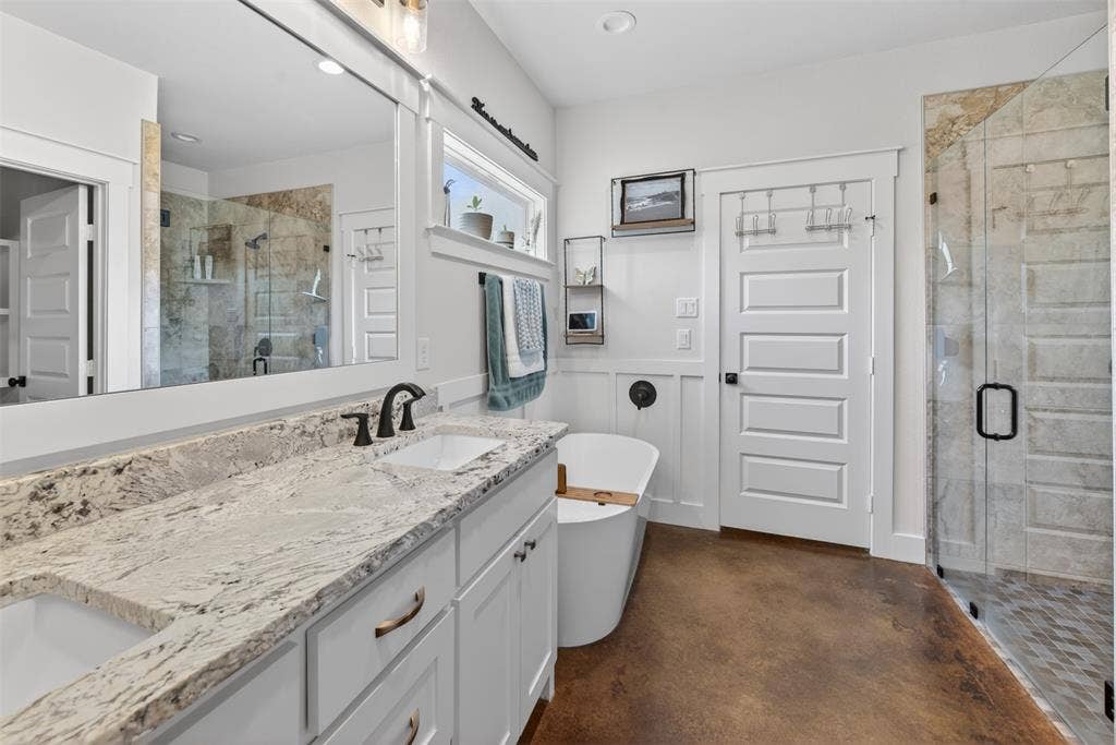 6371 Mill Run Road, Athens, TX 75751 Contemporary bathroom featuring a spacious vanity with a light-toned granite countertop and two sinks, a freestanding soaking tub, and a glass-enclosed shower