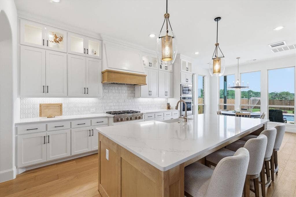 Gourmet kitchen featuring a large central island with seating, pendant lighting, white cabinetry with display uppers, stainless steel appliances, and a tiled backsplash