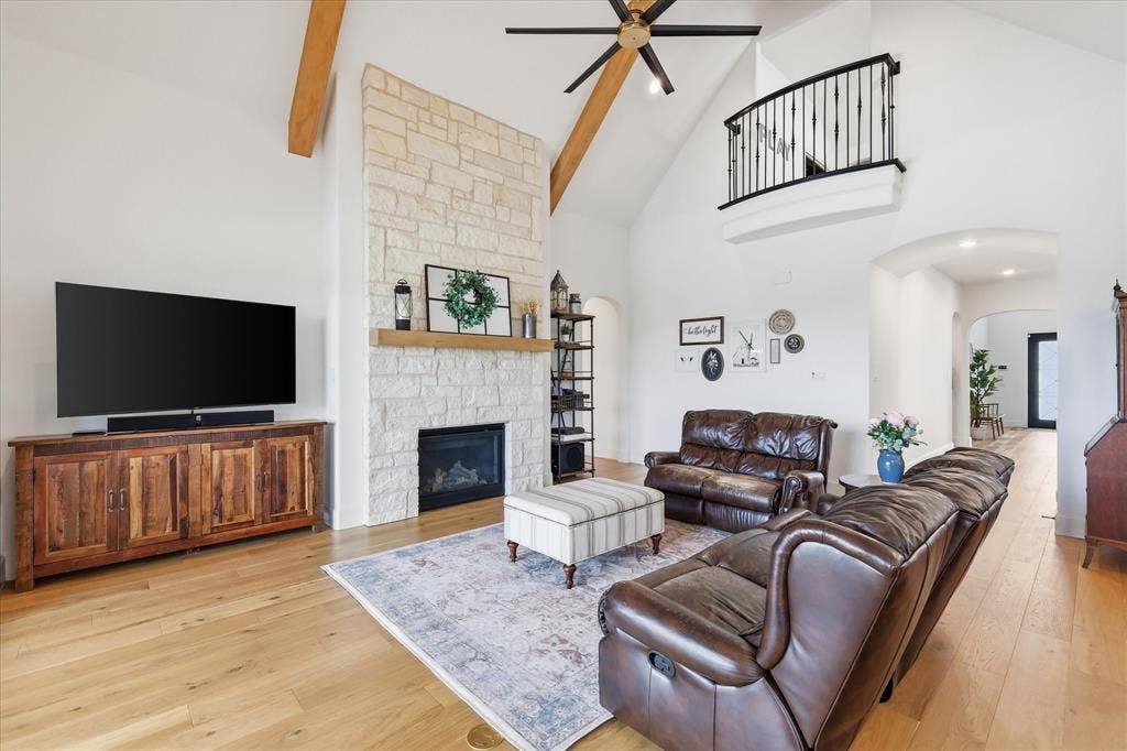 Spacious living area featuring a vaulted ceiling with exposed wood beams, a stone-faced fireplace with a wood mantel, and light wood-finish flooring